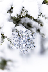 Silver crystal snowflake ornament hanging on a snowy tree branch. Winter background.