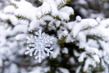 Silver crystal snowflake ornament hanging on a snowy tree branch. Winter background.