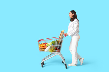 Beautiful young happy woman with full shopping cart on blue background