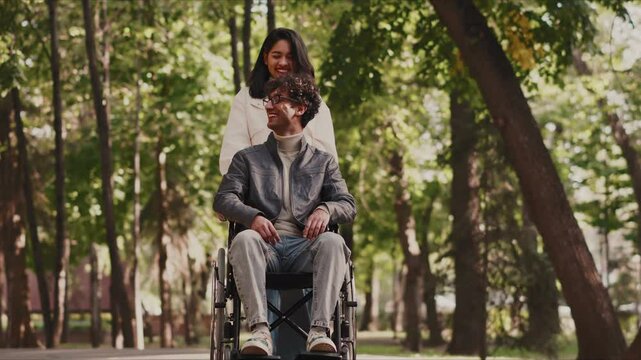 Young woman pushing her disabled boyfriend in a wheelchair in a park