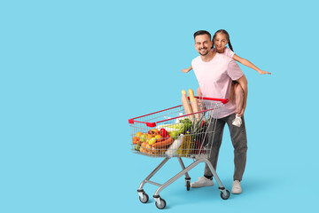 Young happy father and her daughter with full shopping cart having fun on blue background