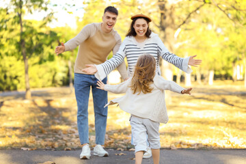 Fototapeta premium Happy family opening arms for hug their daughter in beautiful autumn park