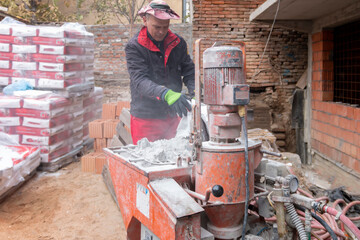 An automatic mixer for mixing dry plaster with water and automatically feeding the finished plaster. A worker pours a bag of dry plaster into the hopper.