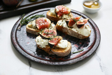 Plate of delicious fig bruschetta with ricotta and blue cheese on white background, closeup