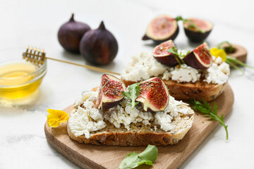 Wooden board of delicious fig bruschetta with ricotta cheese and arugula on white background, closeup