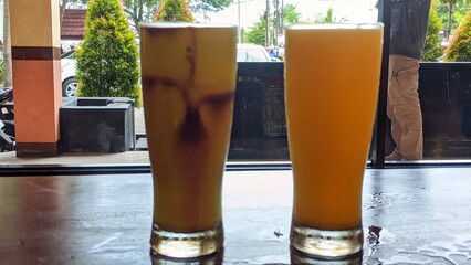 Two tall glasses filled with different drinks are placed on a wooden table.