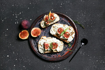 Plate of delicious fig bruschetta with ricotta cheese and arugula on black background