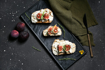 Board of delicious fig bruschetta with ricotta cheese on black background