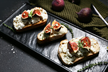 Board of delicious fig bruschetta with ricotta cheese on black background, closeup