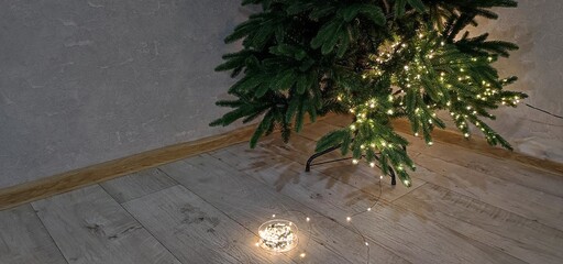 The process of preparing for Christmas and the New Year, decorating the Christmas tree with a garland, the tree is partially decorated, a garland lies nearby.