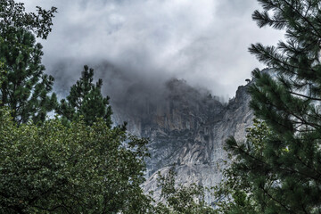 Tall granite cliffs of Yosemite Park, with clouds drifting around the peaks, providing a ethereal atmosphere