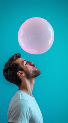 Man blowing a large bubblegum balloon against blue background, playful expression. Fun and leisure concept