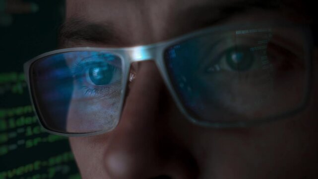 Close-up portrait of focused software engineer wearing eyeglasses looking at computer screen working with big data. Programming code reflecting in glasses. Data science, Machine Learning, AI concept