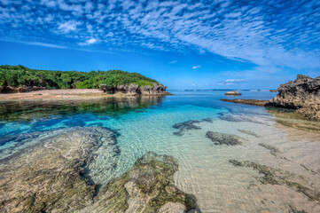 Fototapeta premium Crystal clear waters of Bise Beach, Motobu District, Okinawa main island. White sand beach with coral outcrops and small islands offshore.