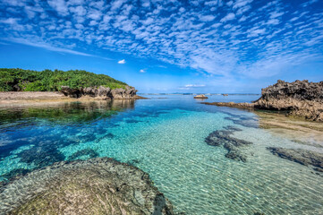 Crystal clear waters of Bise Beach, Motobu District, Okinawa main island. White sand beach with coral outcrops and small islands offshore.