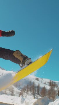 SLOW MOTION CLOSE UP: Extreme snowboarder jumping in big mountain ski resort. Detail of snowboard taking off the kicker in groomed snow park. Snowboarding jump on sunny winter day in snb park