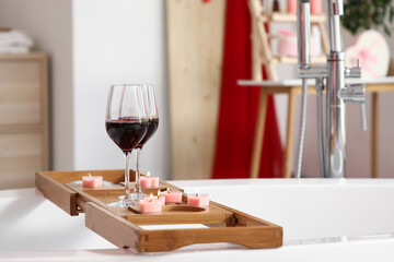 Board with glasses of wine and burning candles on bathtub, closeup. Valentine's Day celebration
