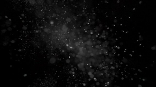 Many white dust particles floating in dark light on empty black background with spotlight from above.