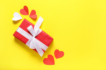 Composition with gift box and paper hearts on yellow background. Valentine's Day celebration