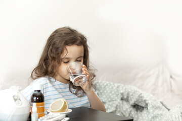 Sick sad little kid girl sits on bed at home and drinking water. Flu season. Healthcare concept.