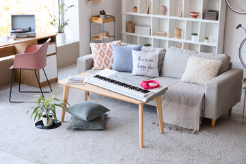 Interior of light living room with sofa, tables and synthesizer