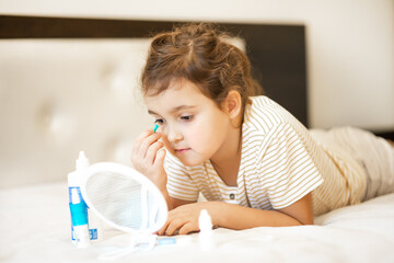 Cute little girl inserting contact lenses into her eye. Vision correction and ophthalmology for...
