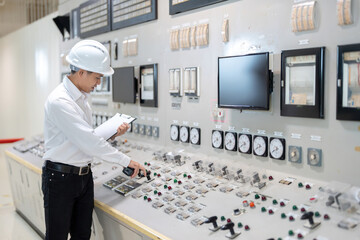 A smart looking male engineer wearing a hard hat and uniform presses a control button in the engine...