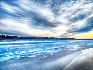 A serene winter sunset over a frozen lake with dynamic clouds reflecting soft evening light