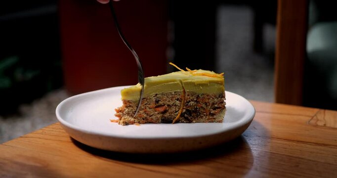 Piece of delicious raw carrot cake with dates and raisins. Topped with mango frosting. Slow-motion video of a piece of vegan carrot cake being eaten with a fork.
