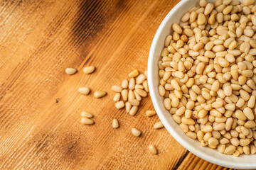 Pine nuts in a white bowl on a wooden background. Space for text.