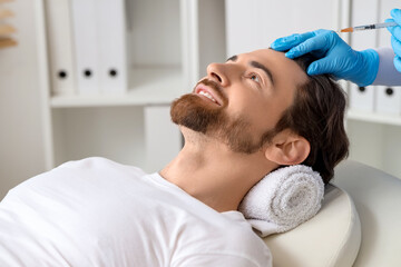 Handsome man receiving injection for hair growth on couch in clinic, closeup