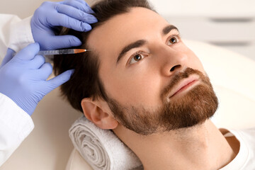 Young man receiving injection for hair growth on couch at trichologist's office, closeup