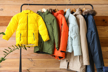 Rack with winter jackets near wooden wall in hall