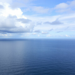 Obraz premium A calm blue sea with rolling waves and a distant island silhouetted against a cloudy sky.