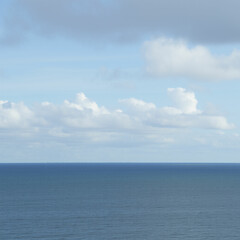 Obraz premium A calm blue sea with rolling waves and a distant island silhouetted against a cloudy sky.