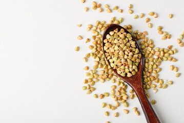 Dietary green buckwheat groats in a wooden spoon close-up isolated on white background copy space