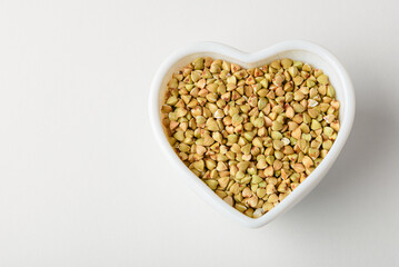 Dietary green buckwheat groats in a heart-shaped bowl isolated on white background, top view with copy space