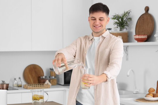 Young man pouring water into glass with lemons in kitchen