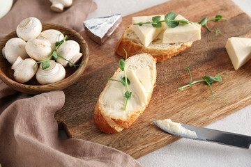 Wooden board with fresh bread, triangles of tasty processed cheese, micro green and mushrooms on...