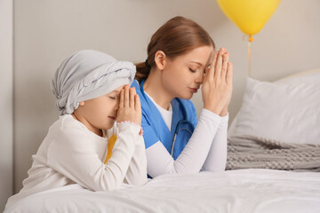 Little girl after chemotherapy with nurse praying in clinic. Childhood cancer awareness concept