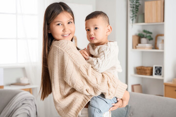 Teenage girl holding her little brother in arms at home