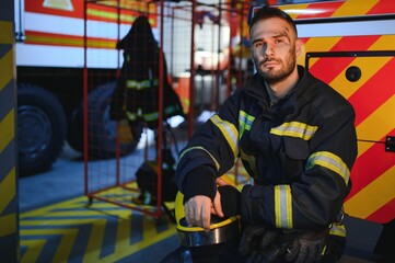 Portrait of a firefighter in a protective suit and a protective helmet standing by a fire engine...