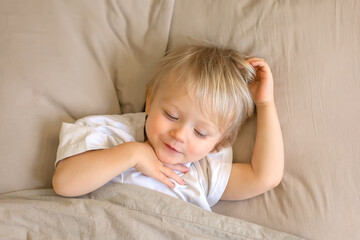 a child with blonde hair laying on a couch with his hand on his head.