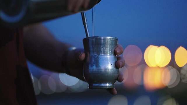 A hand pouring hot water into a mate gourd at night.