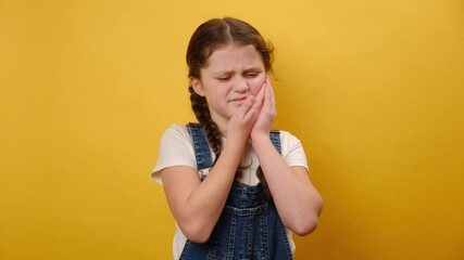 Portrait of sad preteen girl suffering from toothache, isolated on yellow studio background. Anti toothache remedy. Toothache painkiller. Pain relief concept. Dental disease. Plan to visit dentist