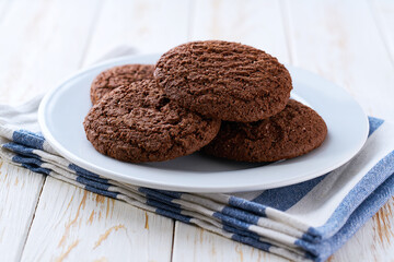 Delicious chocolate cookies in a plate with on a light kitchen table, selective focus.