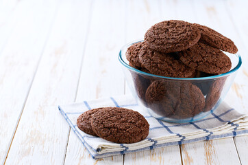Tasty chocolate brownie cookies with cracks  in a clear glass bowl on a white table, selective focus.
