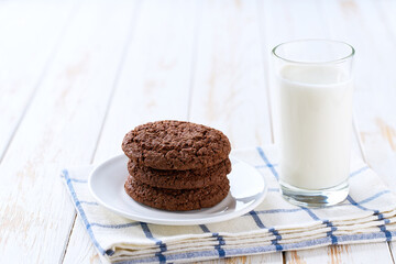 Tasty chocolate brownie cookies with cracks and glass milk on a light kitchen table, selective focus.