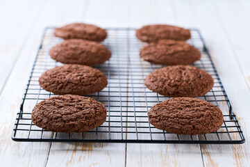 chocolate brownie cookies with cracks in a black wire rack on a white table, close up.