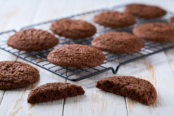 Freshly baked chocolate brownie cookies with cracks cooling on a black wire rack, with in a light kitchen table, selective focus.